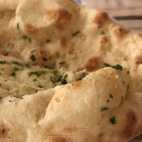 Close-up of fluffy, golden-brown naan bread, sprinkled with green herbs, from Himalayan Restaurant.