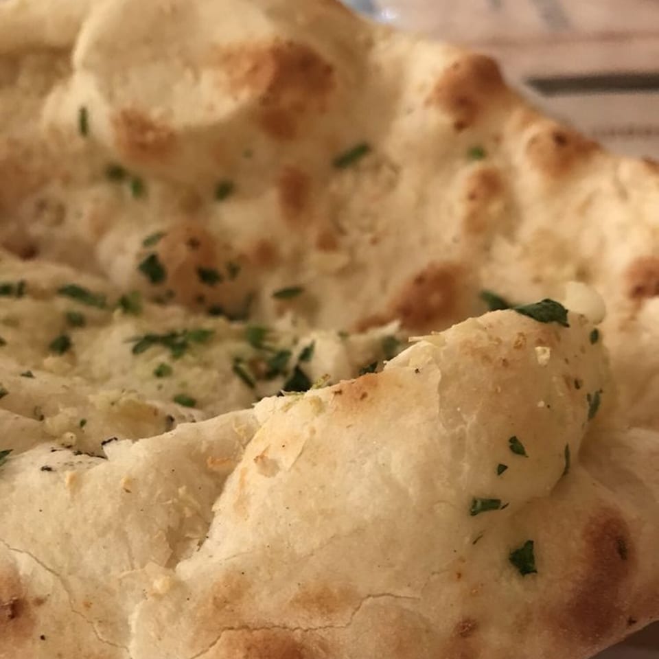 Close-up of fluffy, golden-brown naan bread, sprinkled with green herbs, from Himalayan Restaurant.