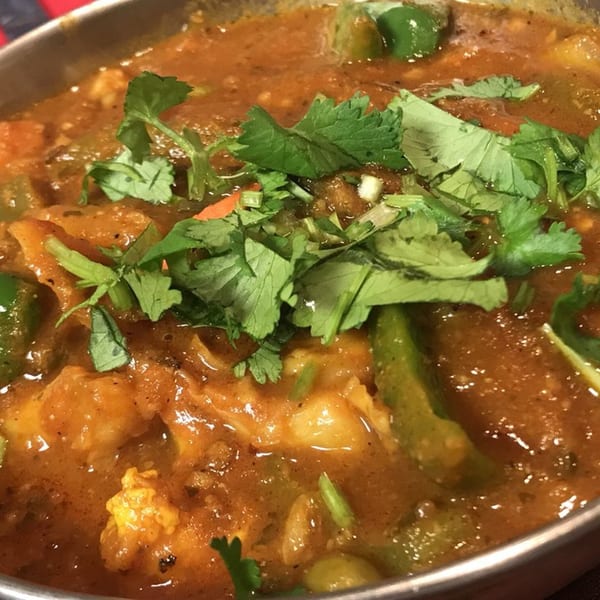 Close-up of a vibrant Indian curry with green peppers and fresh cilantro in a metal bowl.