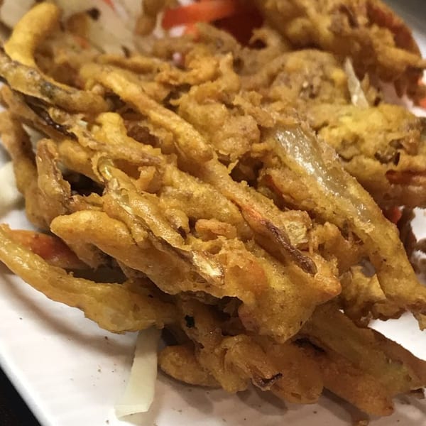 Close-up of golden-brown fried Indian pakora, with visible vegetables and spices, on a white plate.