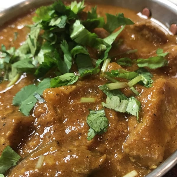 Close-up of Indian curry with chicken pieces and fresh cilantro in a metal bowl.